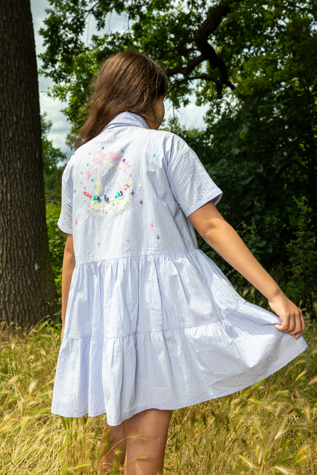 Woman wearing a light blue tiered dress with floral embroidery on the back in an outdoor field