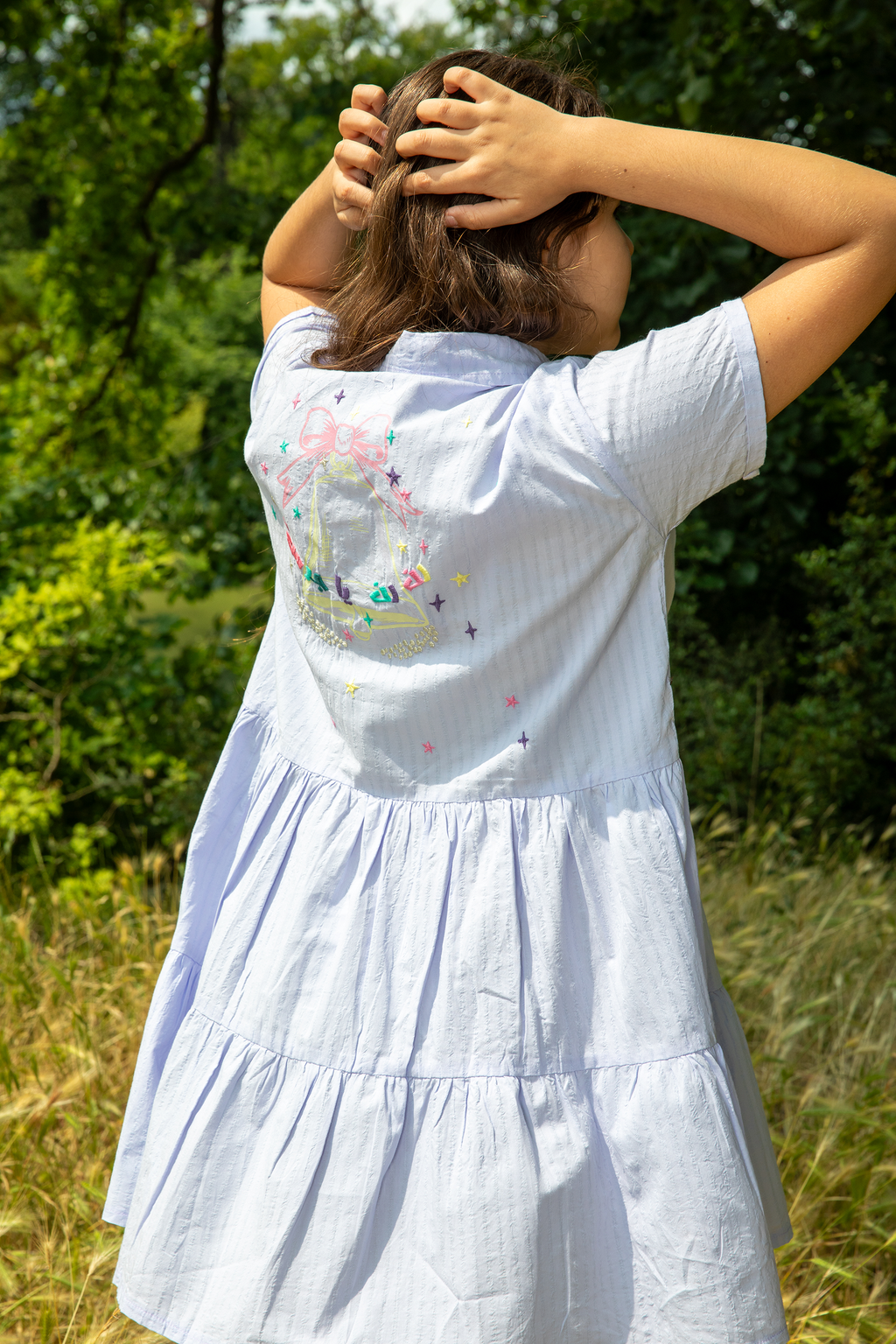Woman wearing light blue tiered dress with colorful embroidery on back standing outdoors