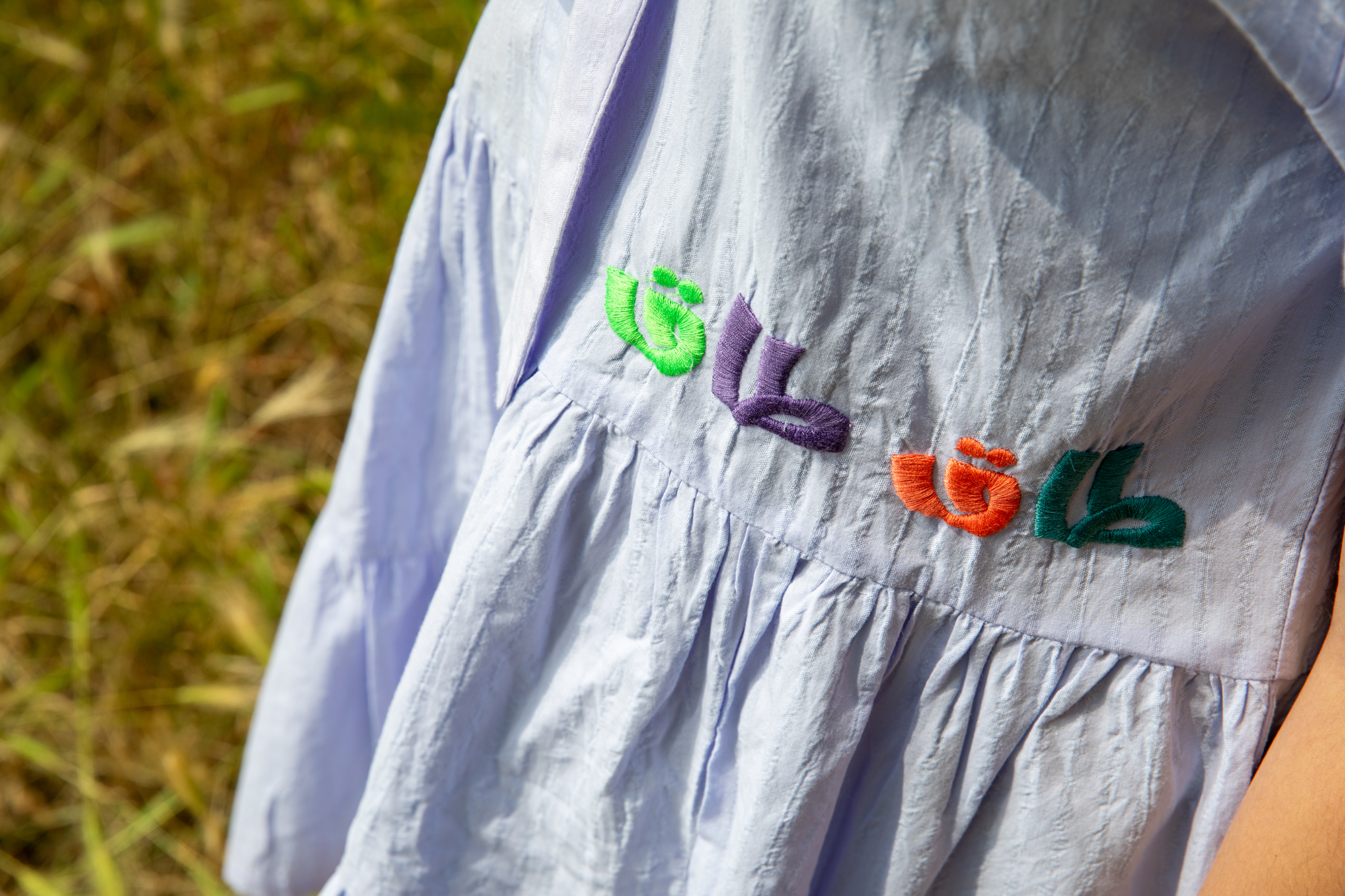 Close-up of white fabric dress with colorful embroidered floral designs by ein-ghein.com