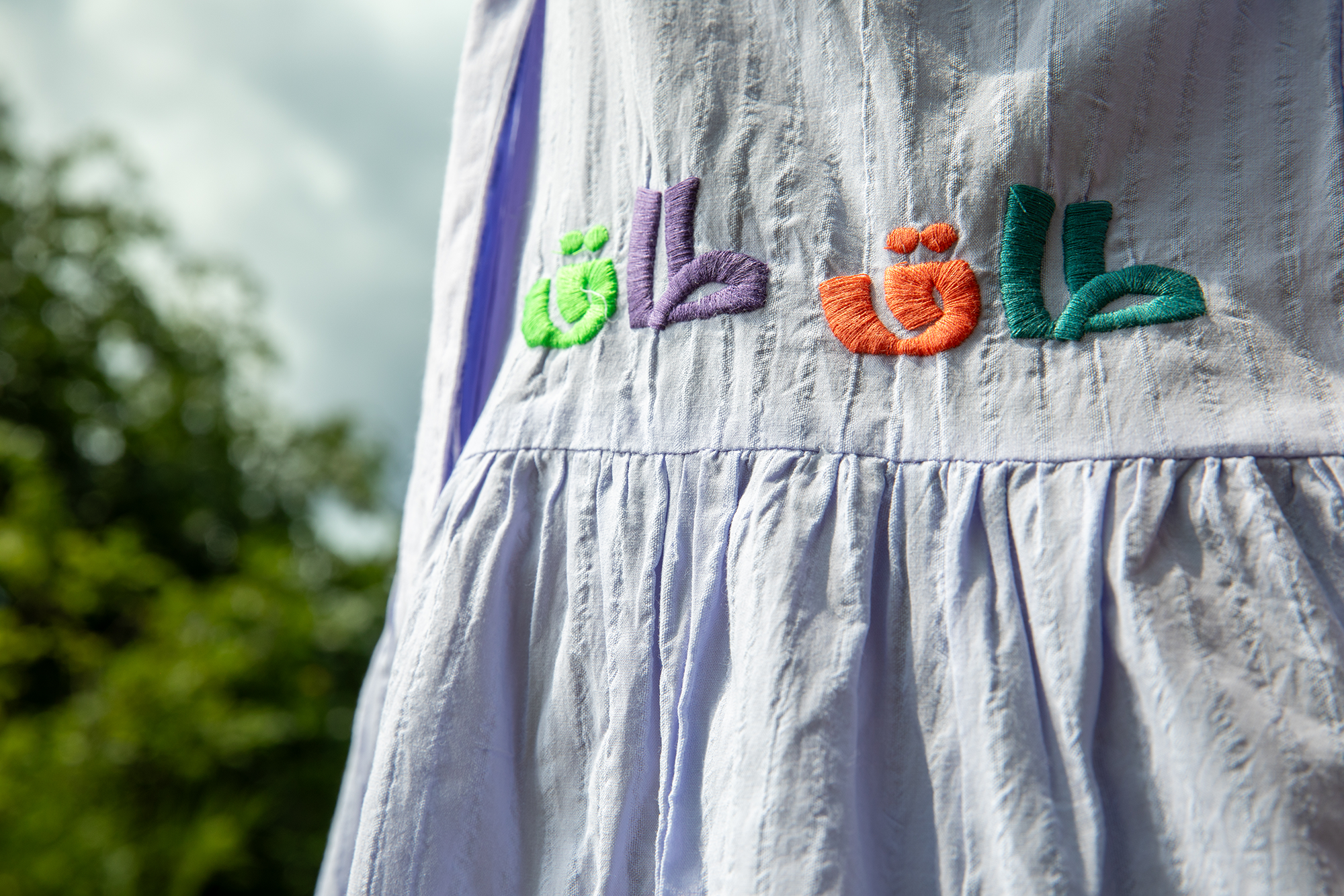 White dress with colorful embroidered Arabic letters in green, purple, orange, and teal on fabric