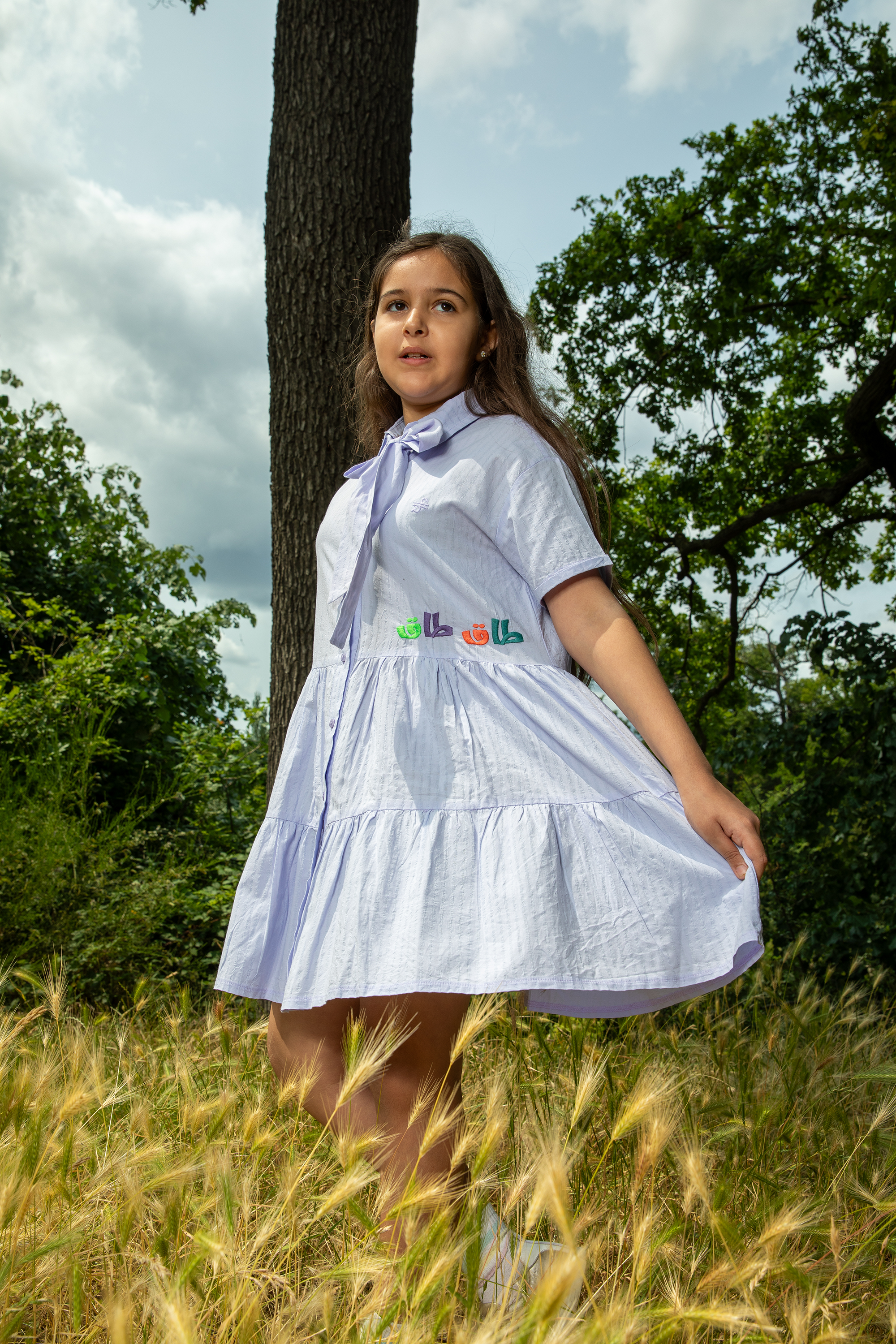 Girl wearing a light purple short-sleeve dress with bow detail standing in a grassy outdoor area